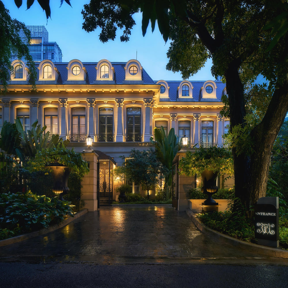 The lit facade of Comte Manoir at dusk, a Parisian-styled residence in Kebayoran Baru with a mansard roof, dormer windows and wrought-iron balconies