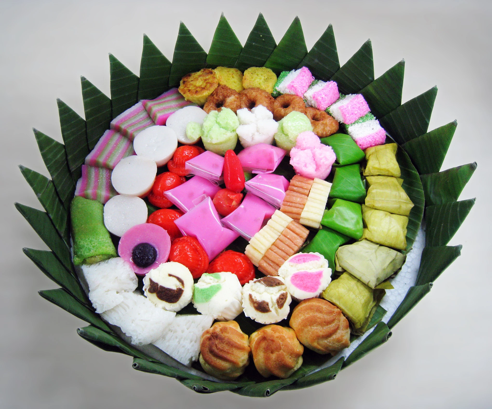 A circular banana-leaf tray of Indonesian kue, arranged in rings of brightly coloured rice-flour and coconut cakes